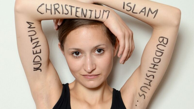 Junge Dame auf deren Armen in Großbuchstaben die Worte "Judentum", "Christentum", "Islam" und "Buddhismus" geschrieben stehen.